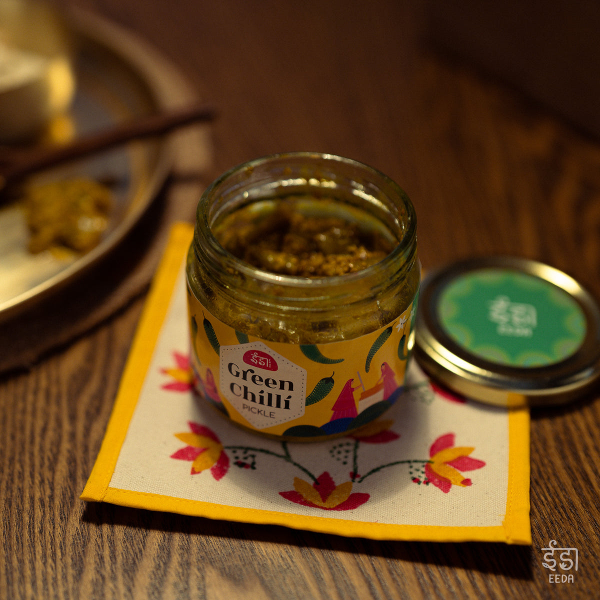 Jar of Eeda Hari Mirch Achar (green chilli pickle) on an embroidered coaster