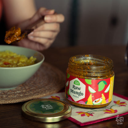 Jar of Eeda Kairi Achar (raw mango pickle) served with a bowl of food